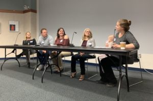 Five adults, one holding a baby, sit on a panel.