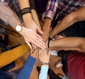 Photo of seven people of different backgrounds standing in a circle with their hands together
